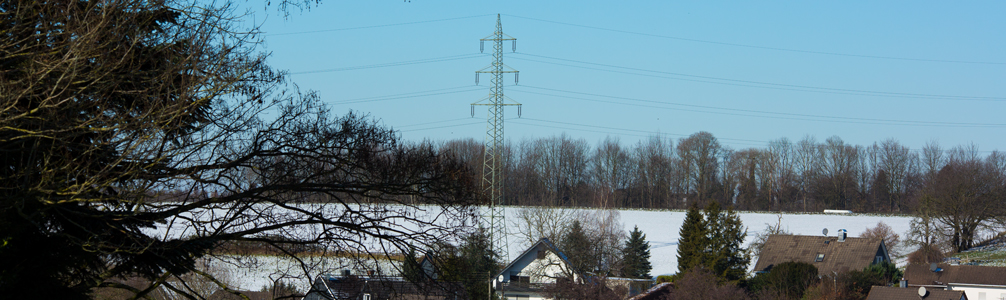 Strommast auf Feld hinter Häusern